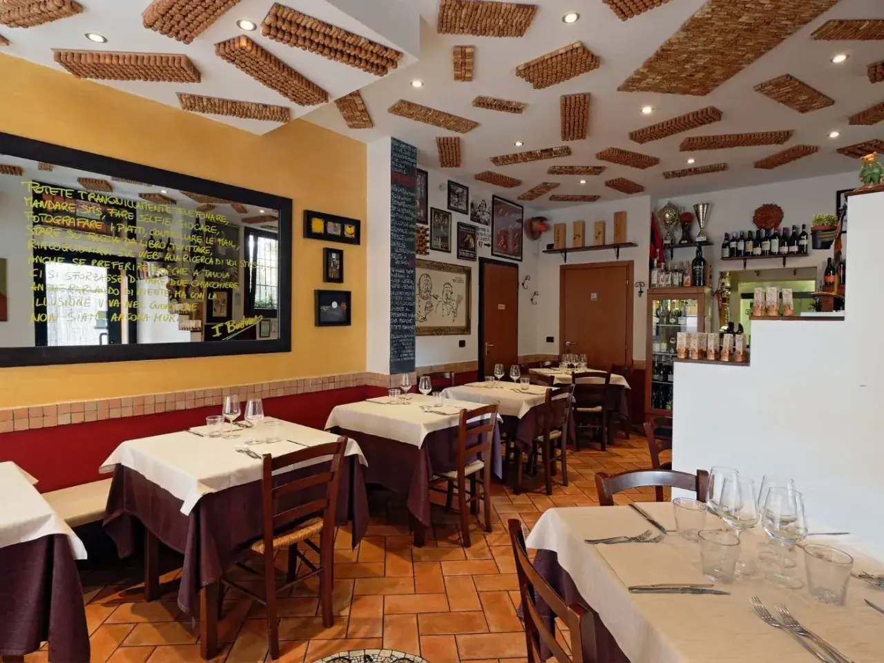Interno di un'accogliente osteria a Bologna, con tavoli apparecchiati e un soffitto decorato con tappi di sughero.