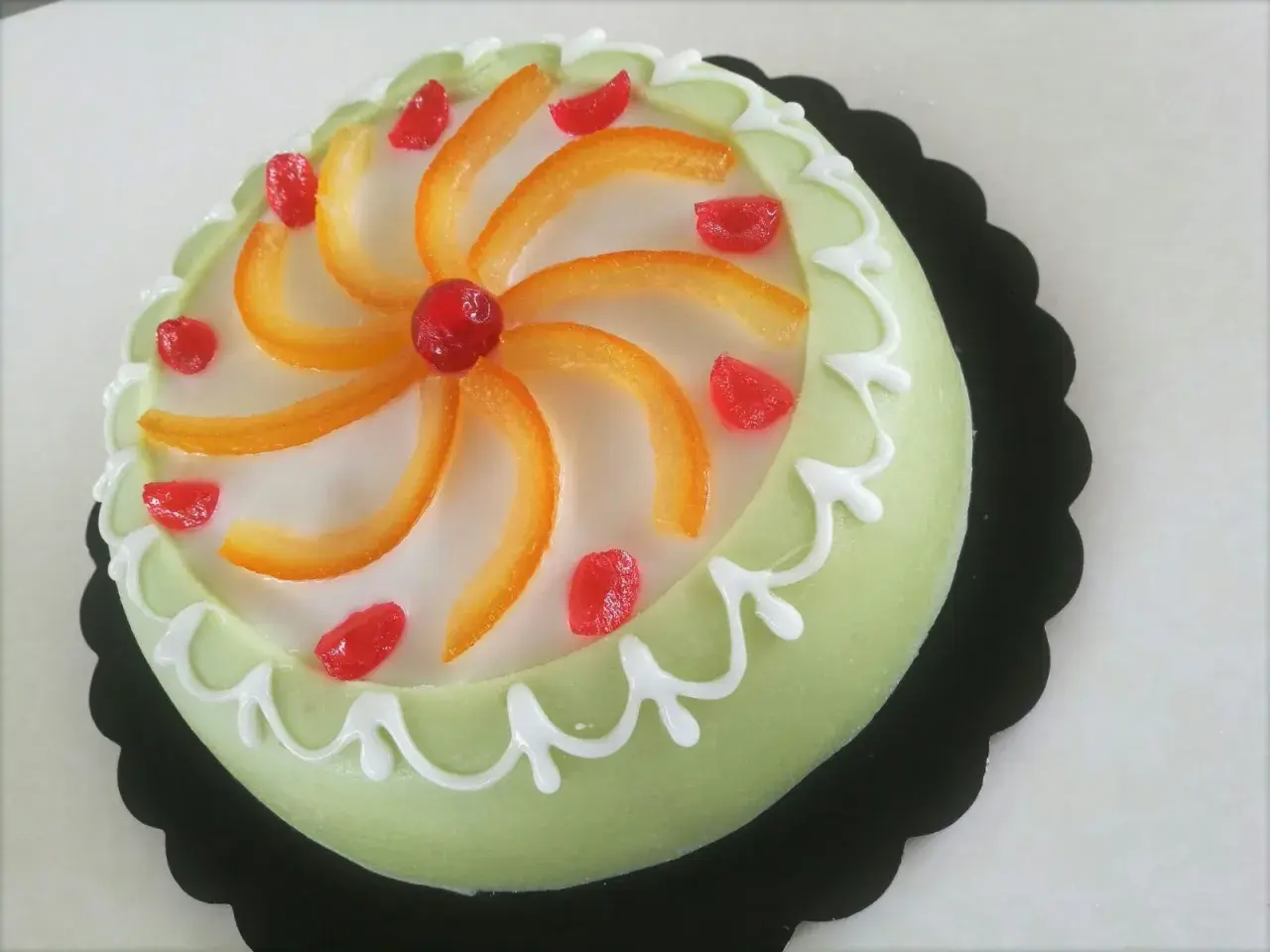 Gâteau sicilien vert pâle glacé, décoré de zestes d'orange, de fruits confits rouges et de glaçage blanc.