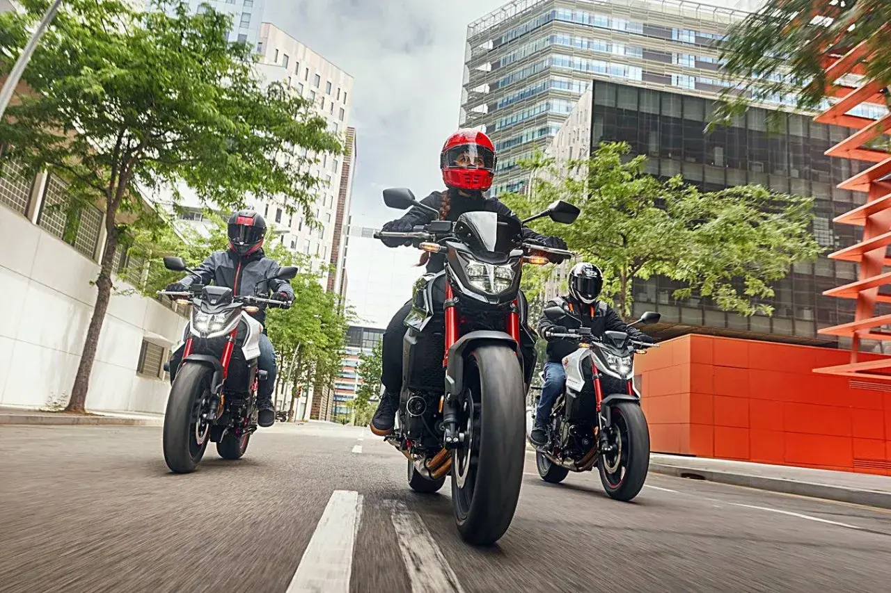 Tres motociclistas con cascos circulan en fila por una calle urbana. Una motocicleta puede circular por el arcén, ofreciendo agilidad entre el tráfico.