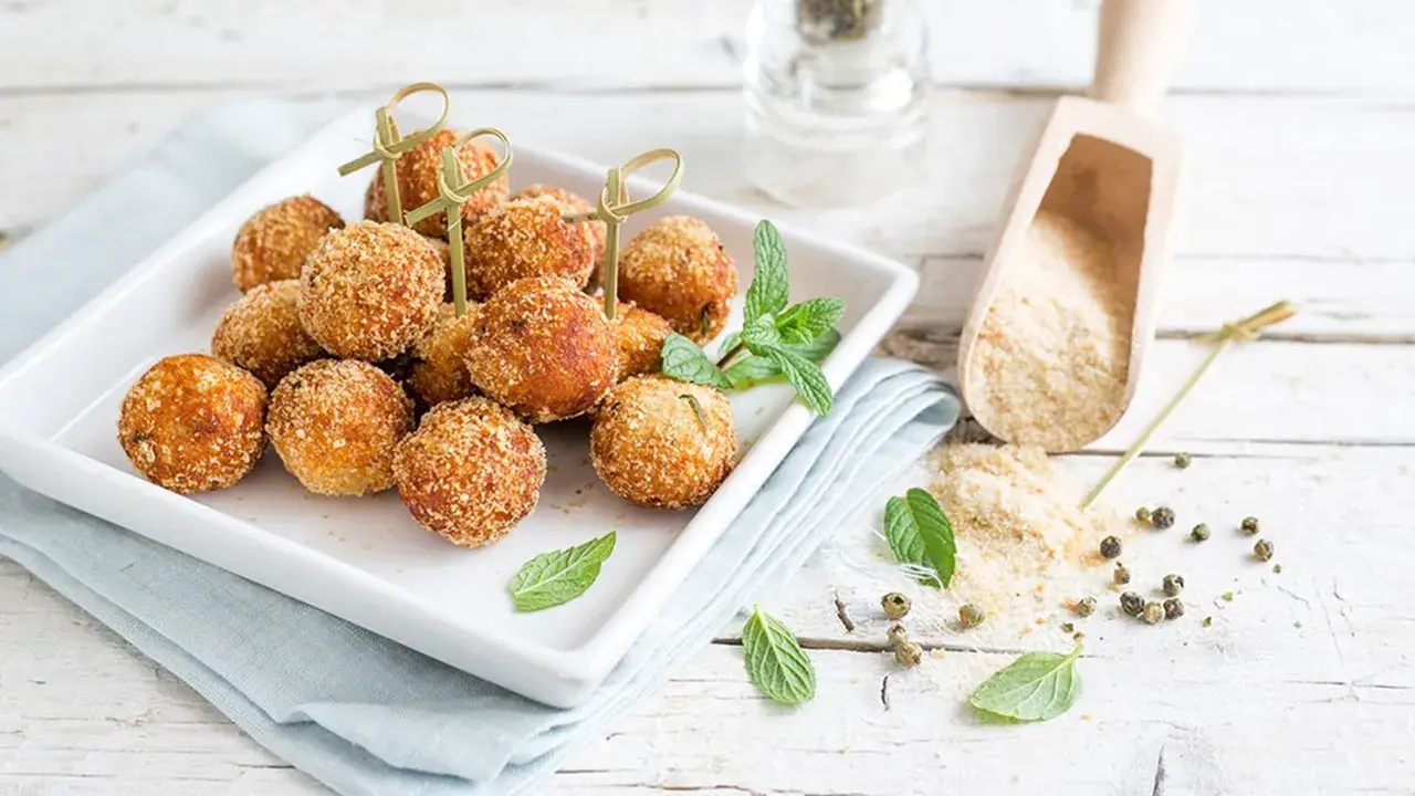 Deliziose polpette tonno e ricotta, dorate e croccanti, servite su un piatto bianco con menta fresca.