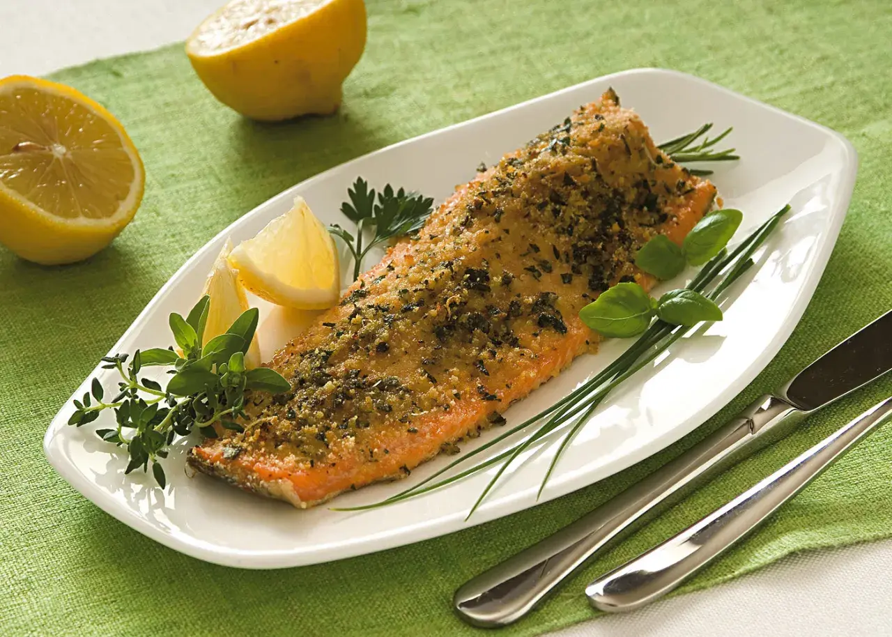 Deliziosa trota salmonata al forno, croccante e profumata, servita con limone e erbe aromatiche fresche.