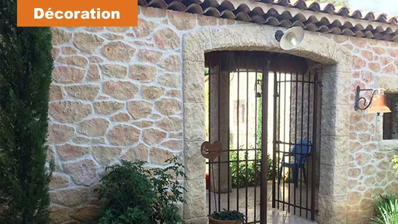 Maison avec un bel enduit pierre apparente, une arche et une grille rouillée.