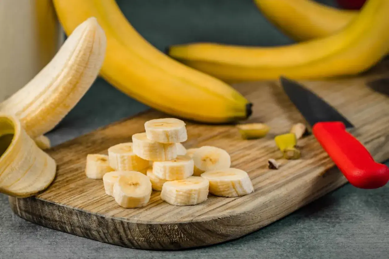 Plasterki banana na desce, idealne na pusty żołądek. Obok leży nóż z czerwoną rączką.