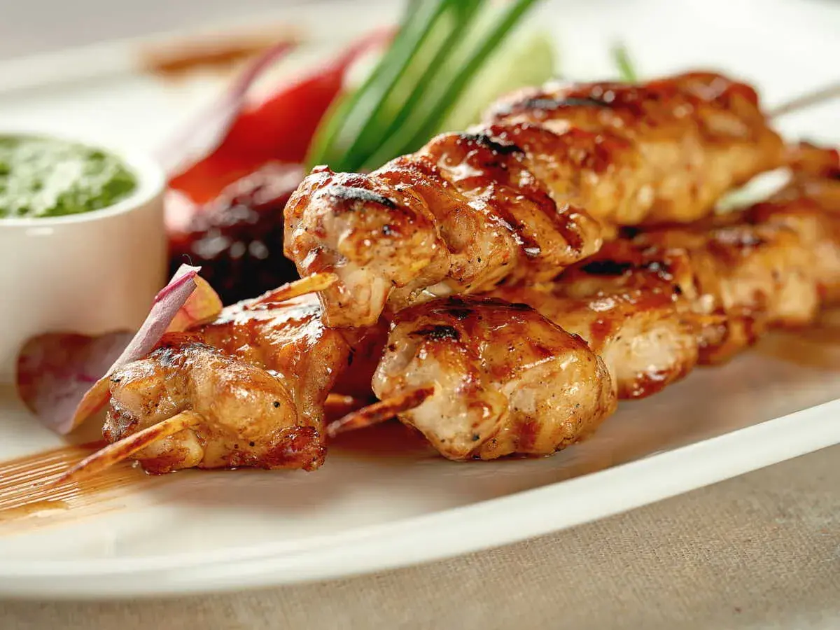 Brochettes de poulet grillées, juteuses et dorées, servies avec une sauce verte et des légumes croquants. Un délice à savourer !