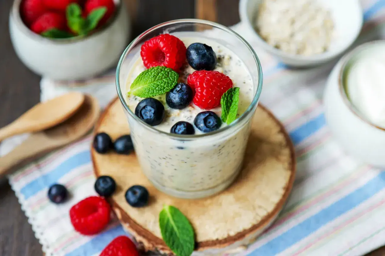 Ein Glas Overnight Oats mit Joghurt, garniert mit frischen Beeren und Minze. Perfekt für ein gesundes Frühstück.