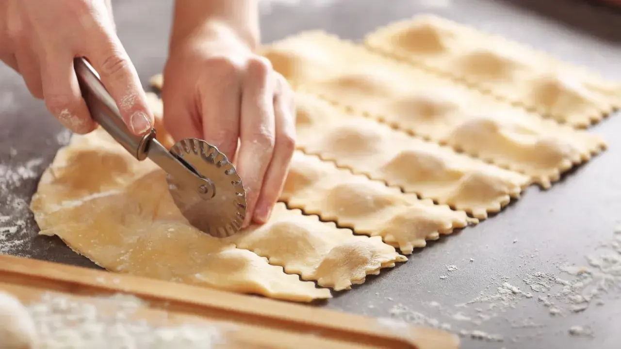 Hände schneiden mit einem Teigrädchen frische Ravioli. So einfach ist ravioli selber machen.