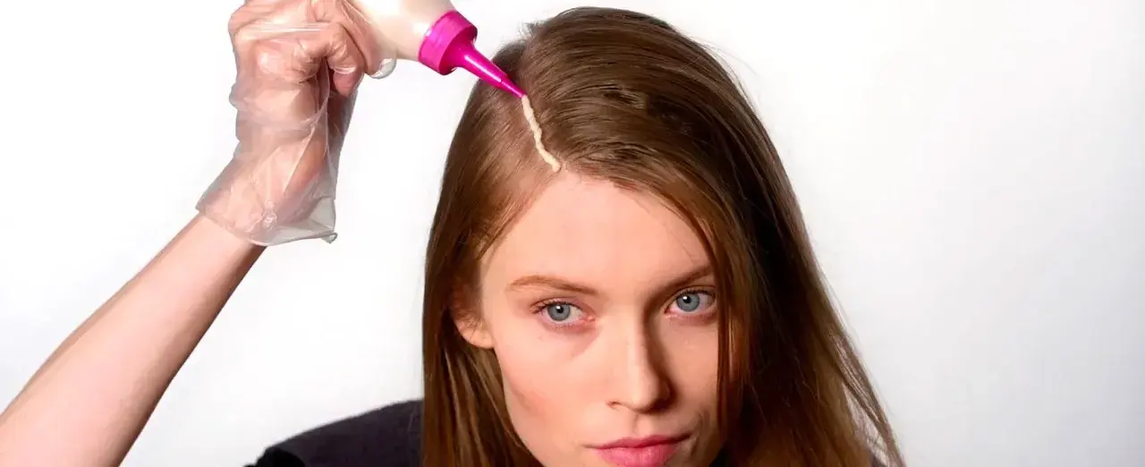 Mujer se aplica tinte en el cabello. Considera los tintes con amoniaco: ventajas y desventajas antes de usarlos.