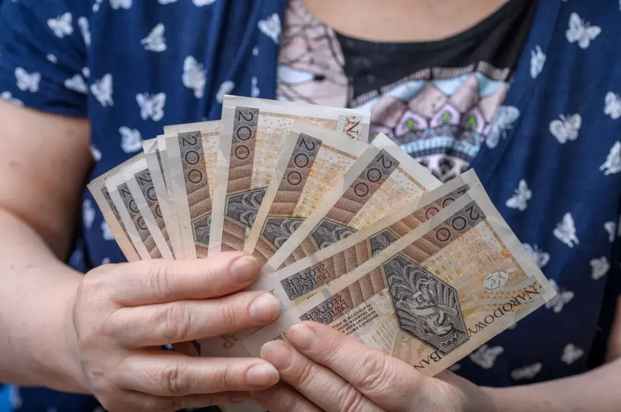 Dłonie trzymające kilka banknotów po 200 zł. Czy to przyszłość renty wdowiej? Zmiany w przepisach mogą wpłynąć na finanse.