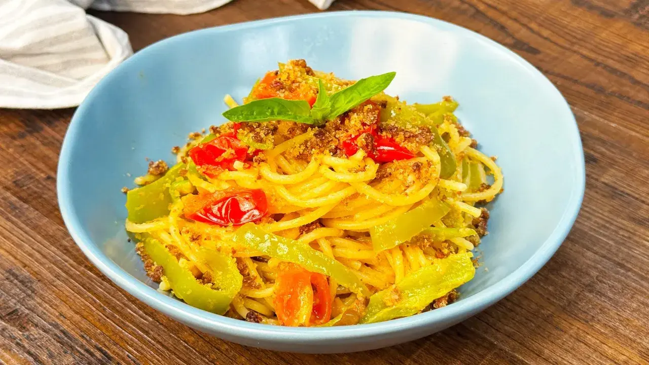 Spaghetti con friggitelli, pomodorini e mollica tostata, guarniti con basilico fresco. Un piatto semplice e gustoso.