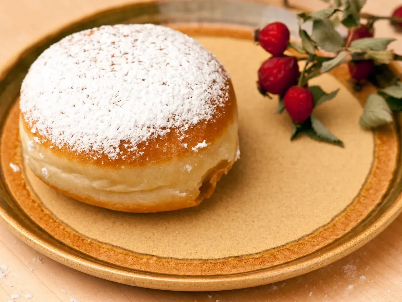 Ein mit Puderzucker bestäubter Krapfen liegt auf einem Teller. Daneben ein Zweig mit Hagebutten. Was ist Hiffenmark?