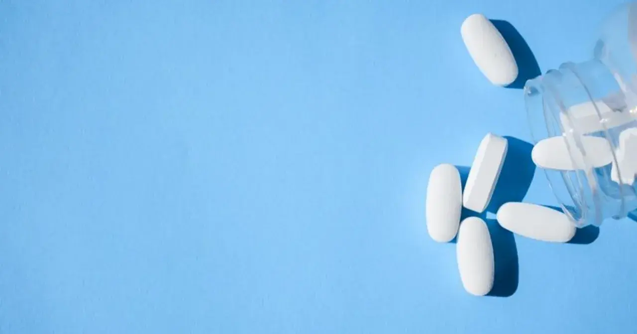 Białe tabletki, w tym oxycodone, wysypują się z przezroczystego pojemnika na niebieskim tle.