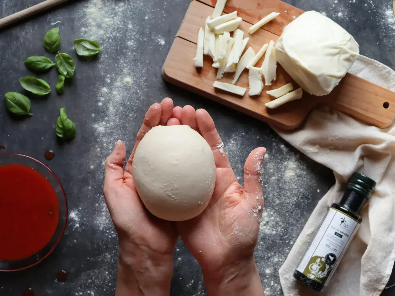 Hände halten Teigkugel für Caputo Nuvola Rezept. Mozzarella, Basilikum und Tomatensauce liegen bereit.