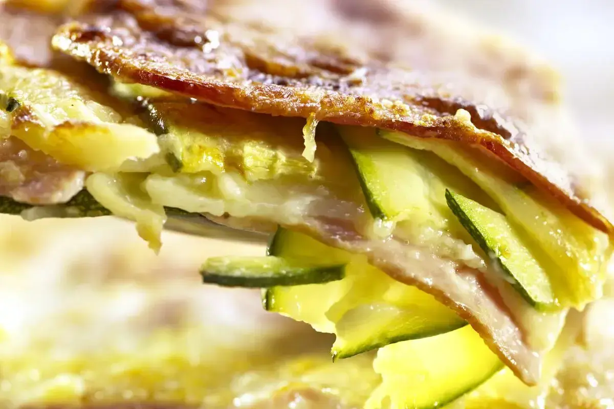 Una fetta di parmigiana di zucchine bianca, con strati di zucchine, formaggio filante e una crosticina dorata.