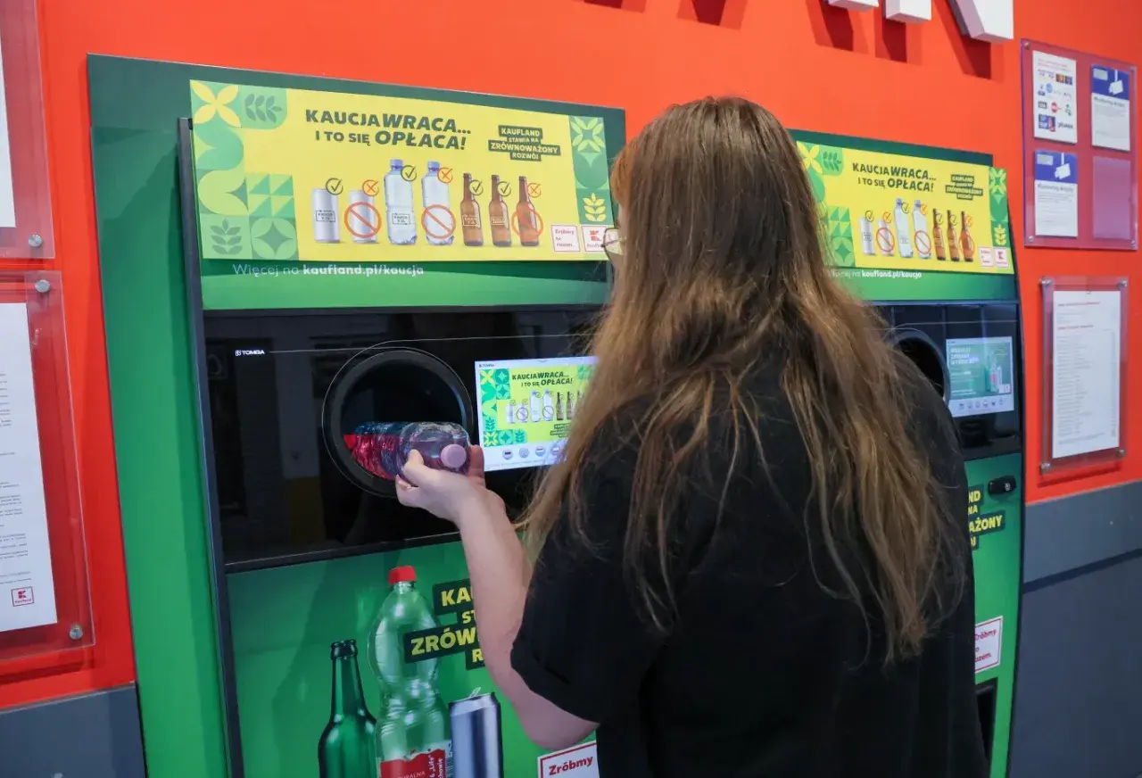 Kobieta wrzuca plastikową butelkę do automatu, który obsługuje system kaucyjny. To ekologiczne rozwiązanie, które zwraca pieniądze.