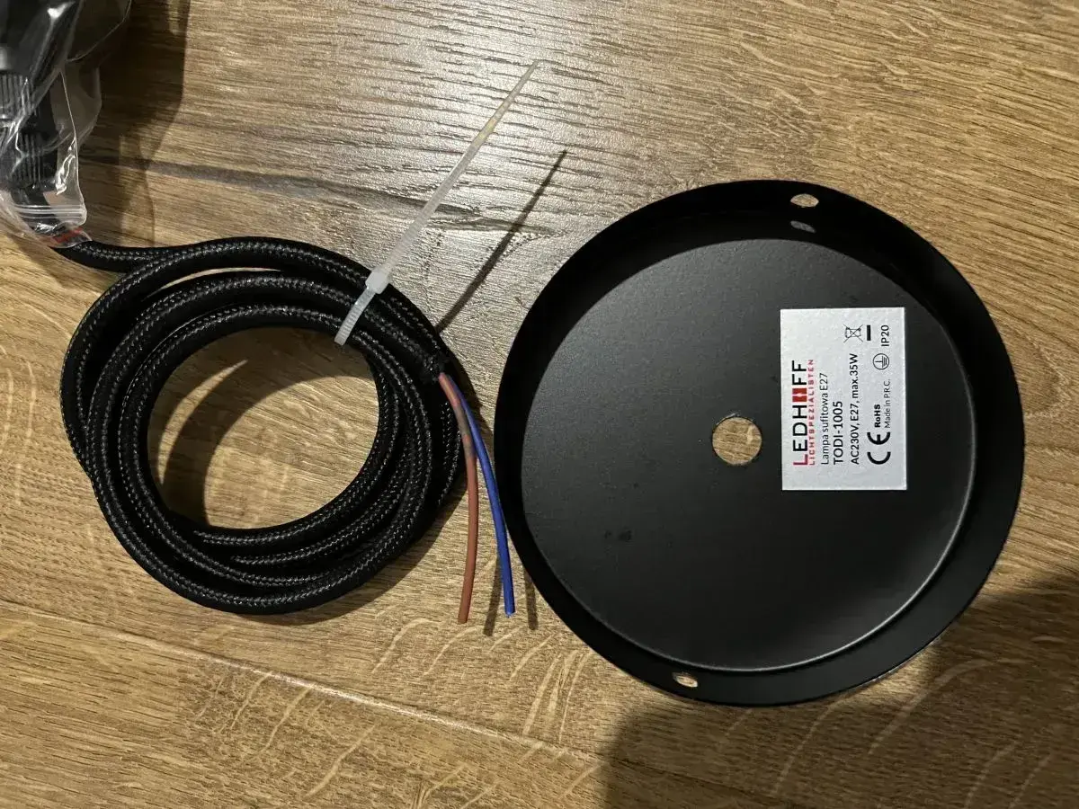Czarny, pleciony kabel z kolorowymi żyłkami obok czarnej rozety sufitowej LEDHOFF.