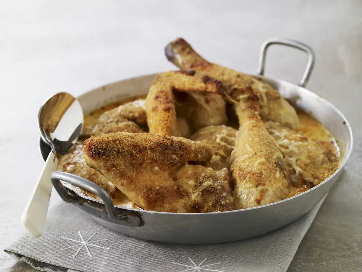 Un plat de poulet Gaston Gérard gratiné, doré et croustillant, servi dans un plat en métal avec une cuillère.