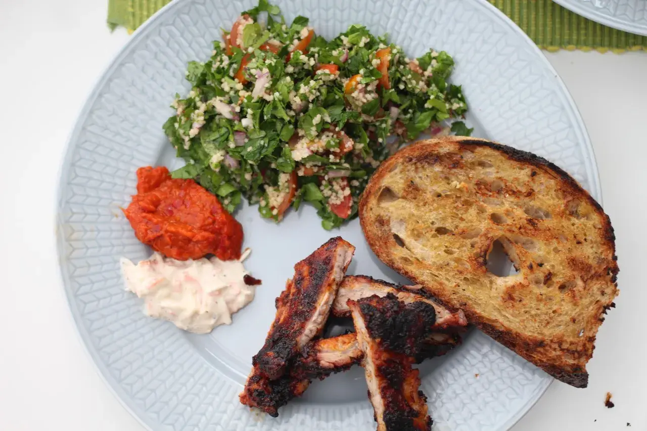En tallrik med grillade revbensspjäll, rostat bröd, en krämig sallad och en fräsch tabbouleh. Perfekt för ett somrigt tabbouleh recept.