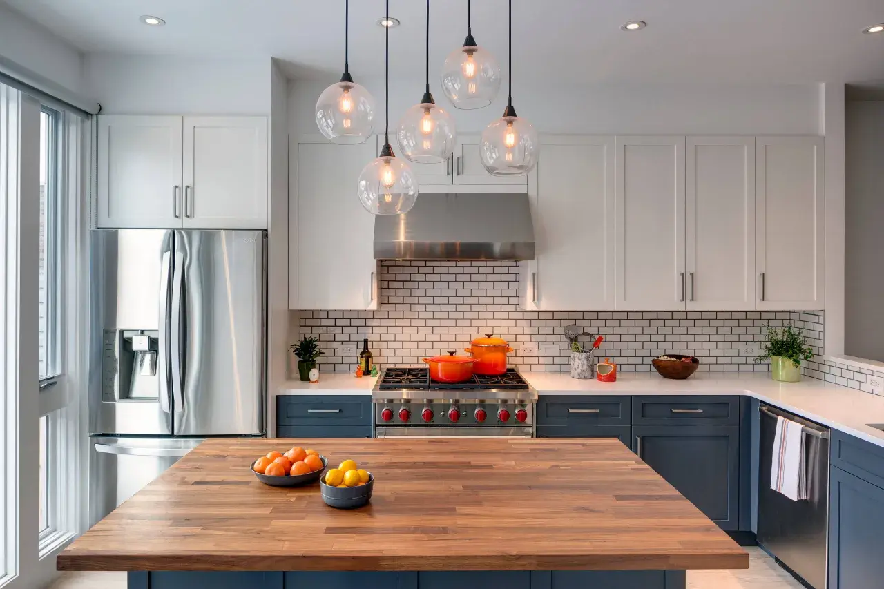 Cucina moderna con isola in legno, elettrodomestici in acciaio e pensili bianchi. Un modo per abbellire una cucina moderna è con tocchi di colore, come le pentole arancioni sul piano cottura.