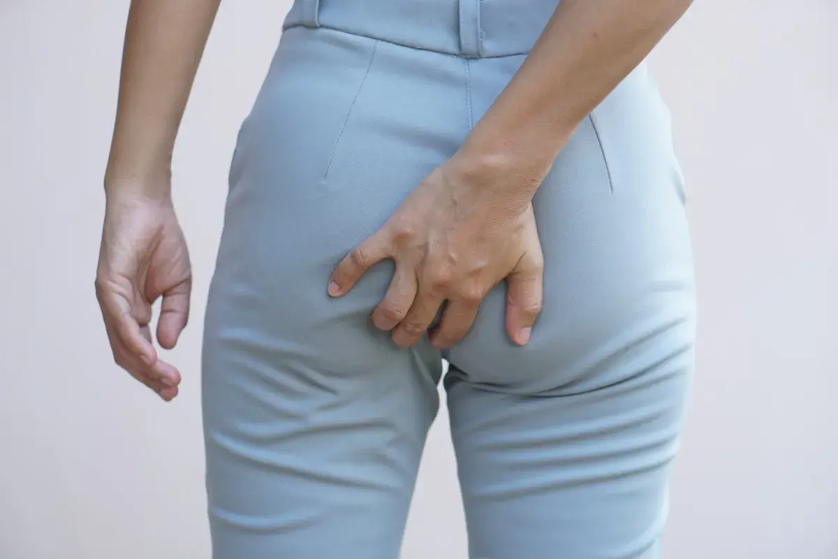 Mano che si gratta il **prurito fondoschiena** attraverso i pantaloni grigi.