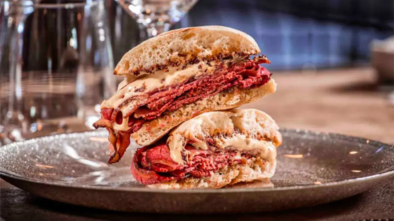 Mollete de pastrami con abundante carne curada y salsa cremosa, apilado en un plato oscuro.