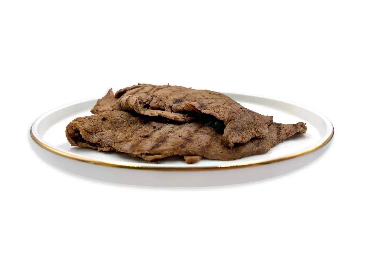 Piatto di paillard di manzo grigliato, sottili fettine di carne con striature scure, servite su un piatto bianco con bordo dorato.