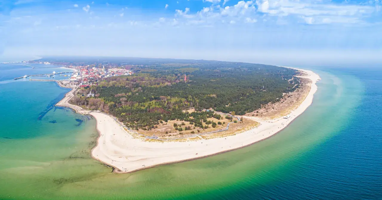 Malownicze wybrzeże pomorza gdańskiego z piaszczystą plażą, lasem sosnowym i miasteczkiem nad zatoką.
