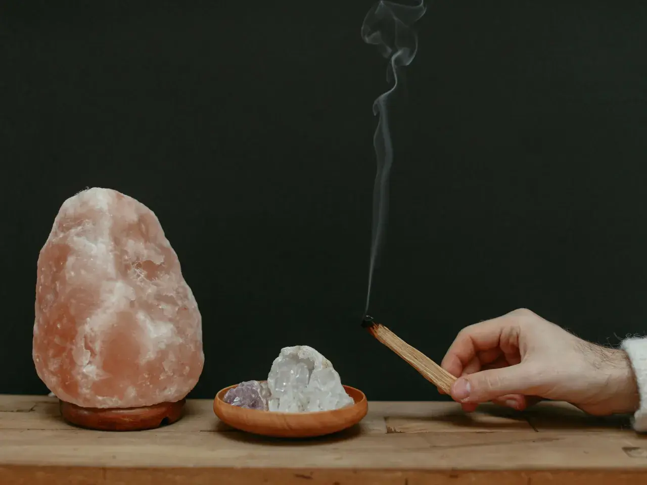 Lámpara de sal rosa, cristales y un palo de incienso humeante.