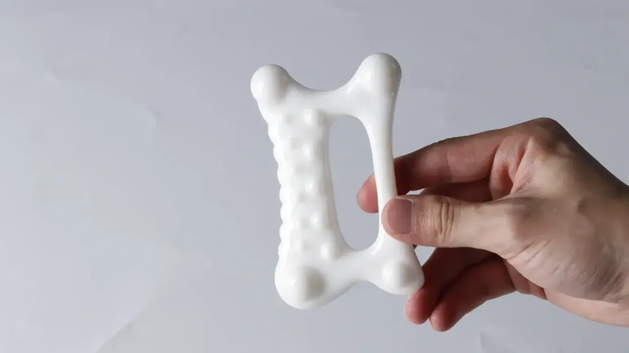 En hand håller ett vitt, benformat verktyg för gua sha massage kropp.