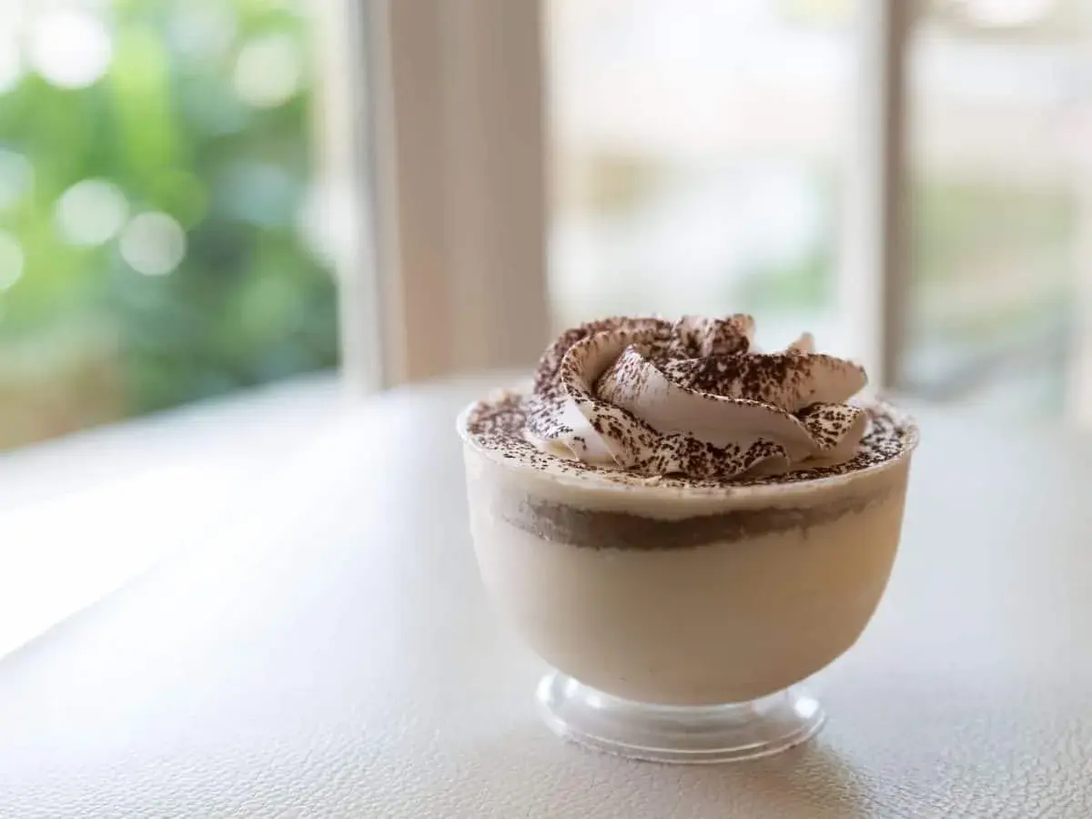 Delicioso mousse de café con crema batida y cacao espolvoreado, servido en un vaso transparente.