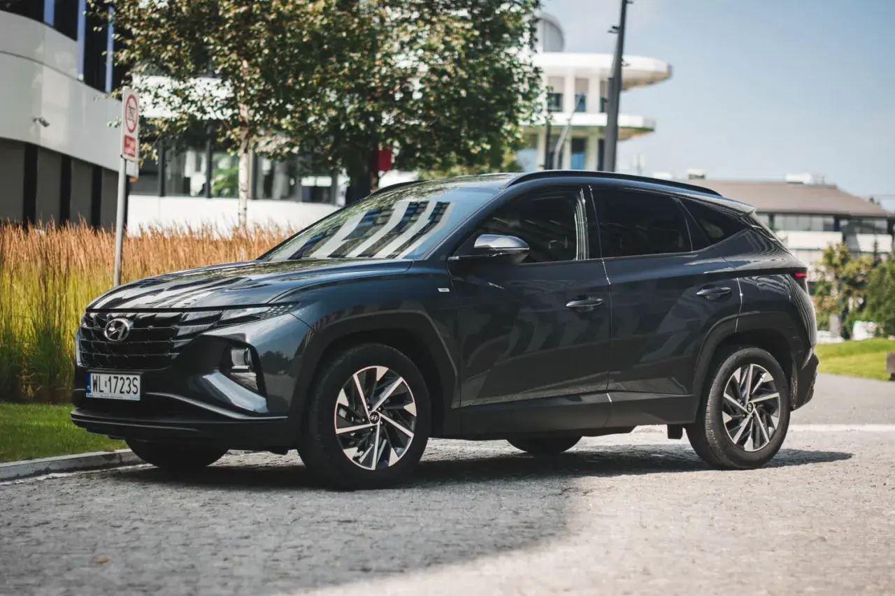 Ciemnoszary Hyundai Tucson 2020 zaparkowany na brukowanej ulicy, z nowoczesnym budynkiem w tle.