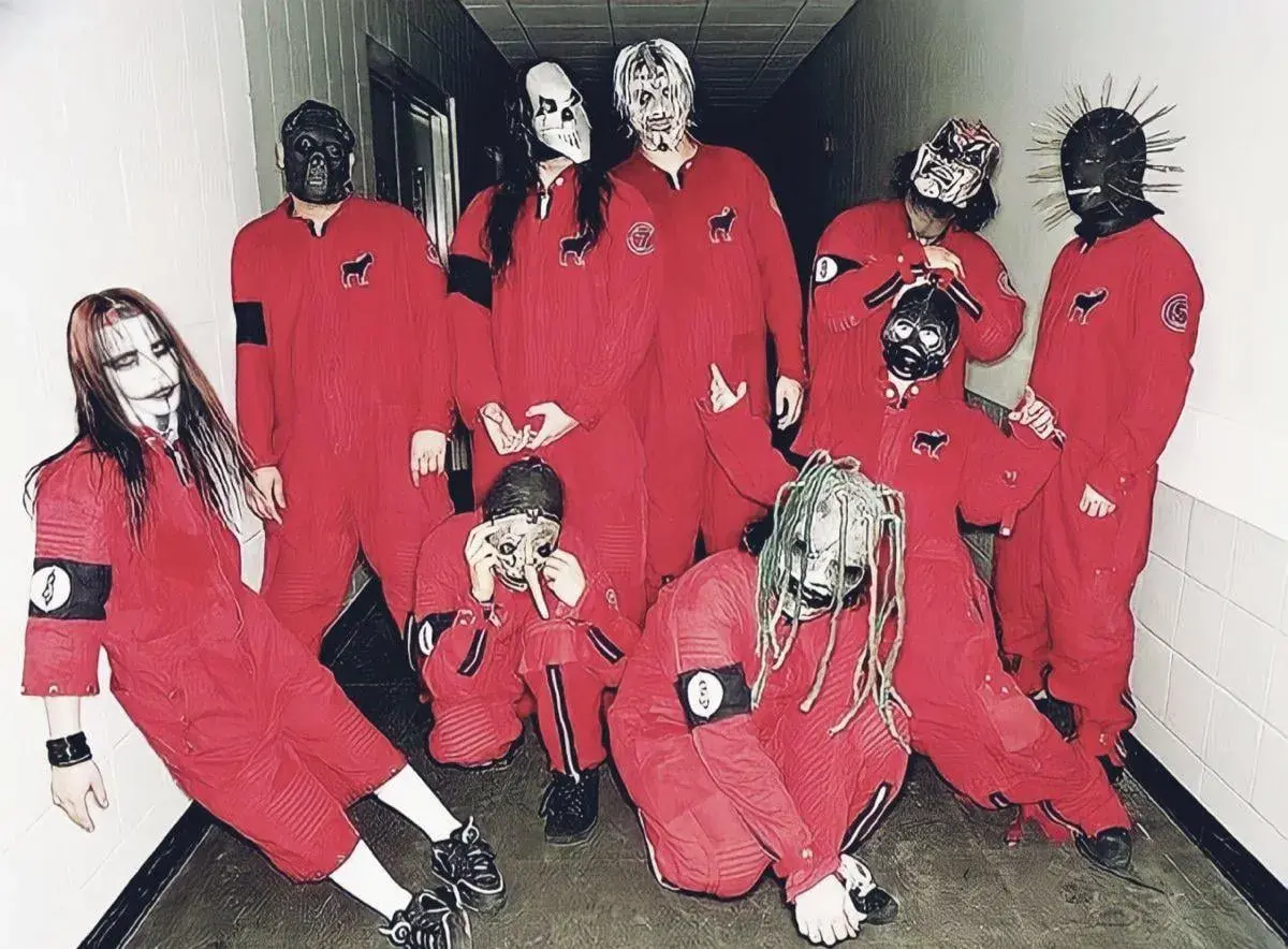 Zespół Slipknot w czerwonych kombinezonach i charakterystycznych maskach, pozuje do zdjęcia w korytarzu.