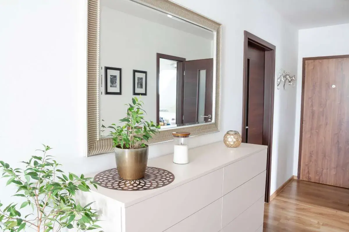 Soluzioni idee piccolo ingresso casa: specchio decorativo, cassettiera chiara, pianta verde e candela creano un'atmosfera accogliente.