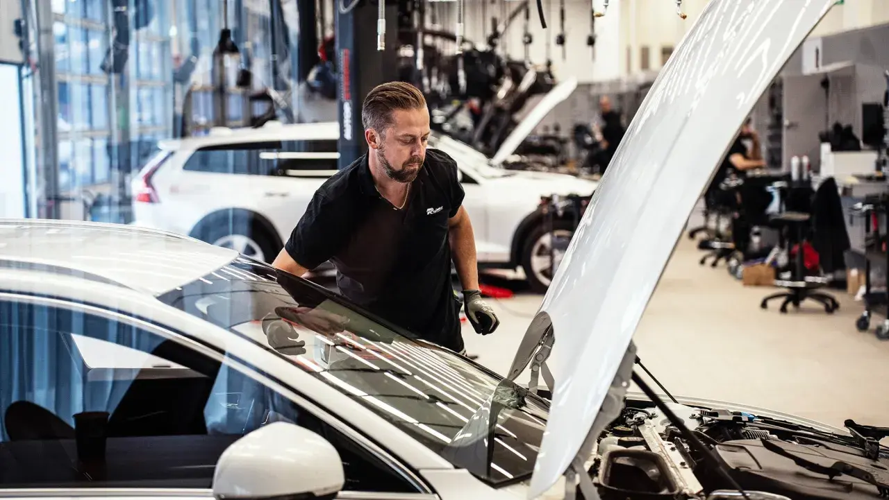 Mekaniker inspekterar en bil med öppen motorhuv. Frågan "hur lång tid tar en bilservice" kan besvaras snabbt med professionell hjälp.