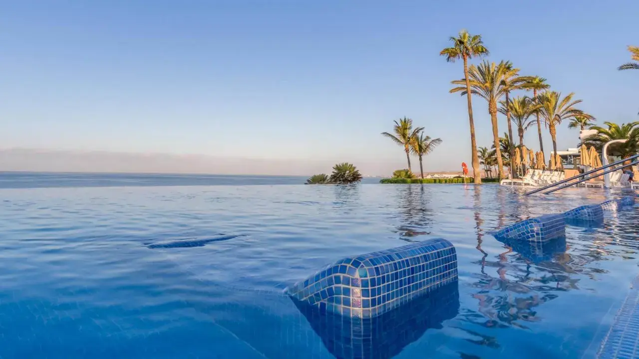 Infinity-Pool mit Blick auf das Meer und Palmen am Riu Palace Meloneras. Entspannung pur im blauen Wasser.