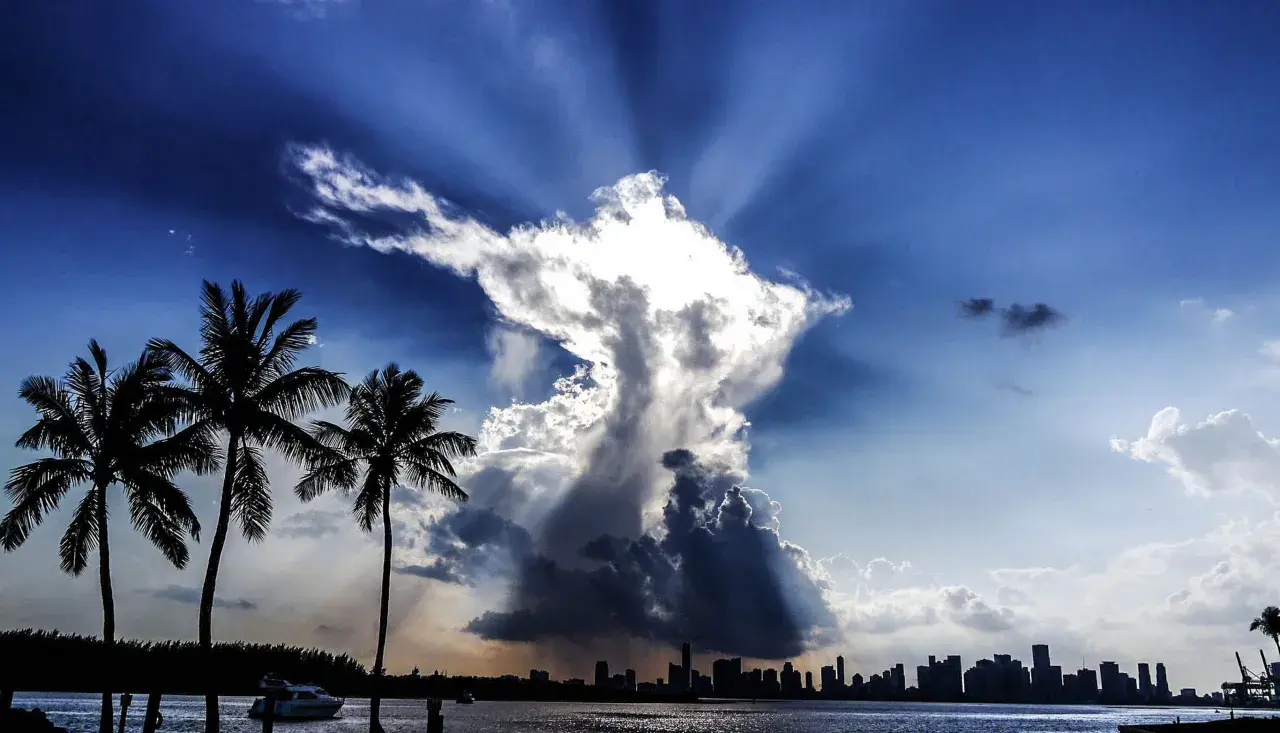 Dramatische Wolkenformationen im Himmel, die an eine engelhafte Gestalt erinnern, über einer Stadtkulisse mit Palmen. Ein Zeichen des Christentums?