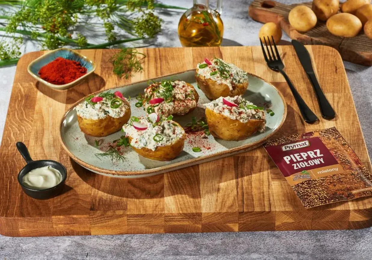 Pieczone ziemniaki z gzikiem i ziołami, udekorowane rzodkiewką i szczypiorkiem. Obok miseczka z majonezem i przyprawa.
