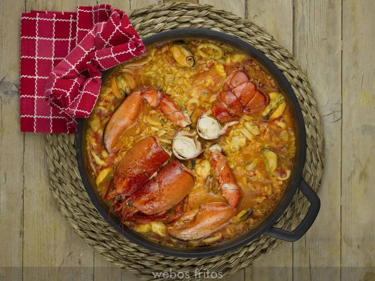 Paella de marisco con langosta, mejillones y calamares, servida en una paellera sobre una esterilla de mimbre.