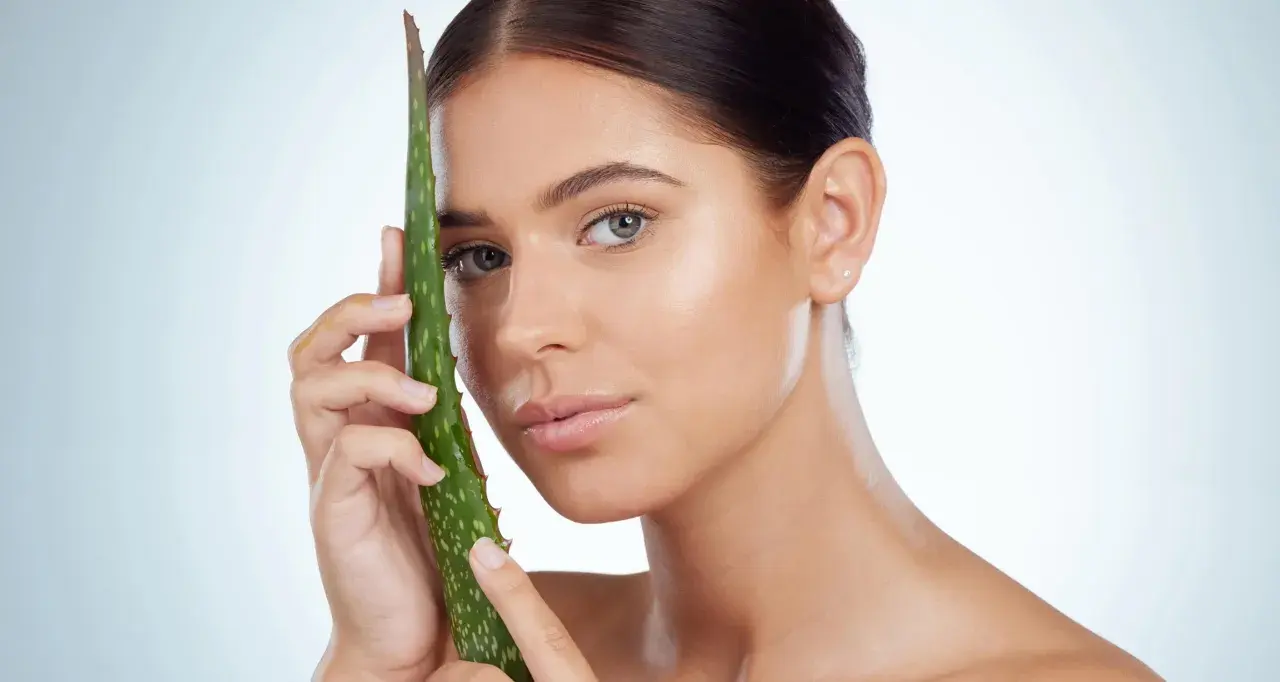 Una mujer joven con piel radiante sostiene una hoja de aloe vera, demostrando que el aloe vera es bueno para la cara.