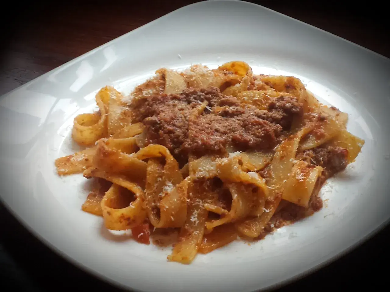 Pappardelle ragu z parmezanem na białym talerzu.