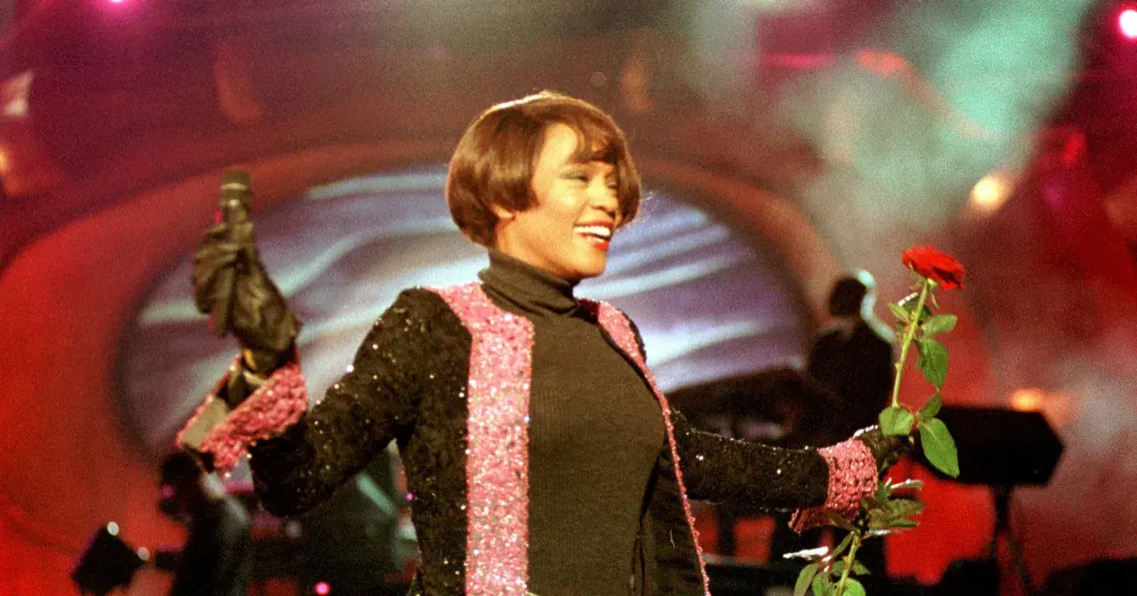 Whitney Houston w Polsce, z mikrofonem i czerwoną różą, w błyszczącej marynarce.