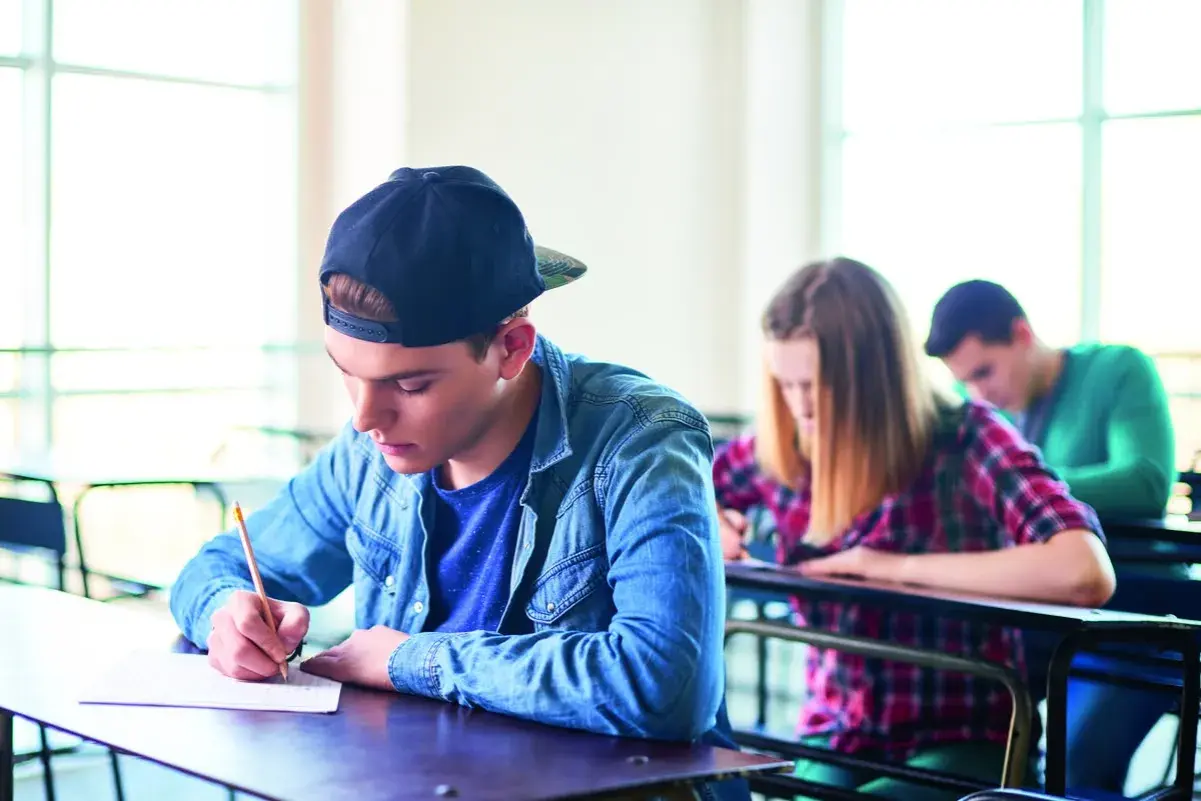 Ragazzo con cappellino scrive concentrato durante un esame. Il suo **did inglese** è importante per il futuro.