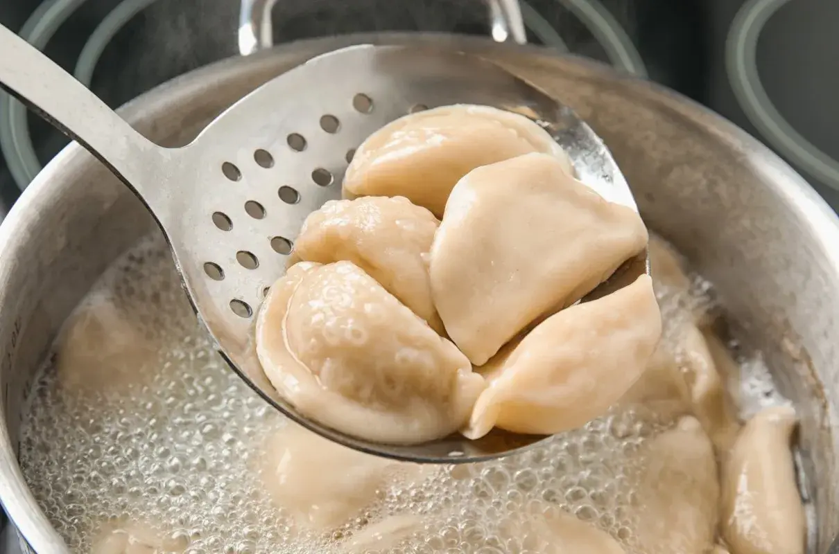 Gorące pierogi z serem, gotowane według przepisu babci, wyjmowane łyżką cedzakową z bulgoczącego garnka.