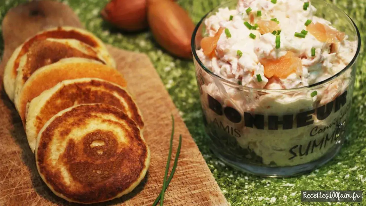 Petits blinis dorés accompagnant un délicieux verre de rillettes de saumon, parsemé de ciboulette fraîche.