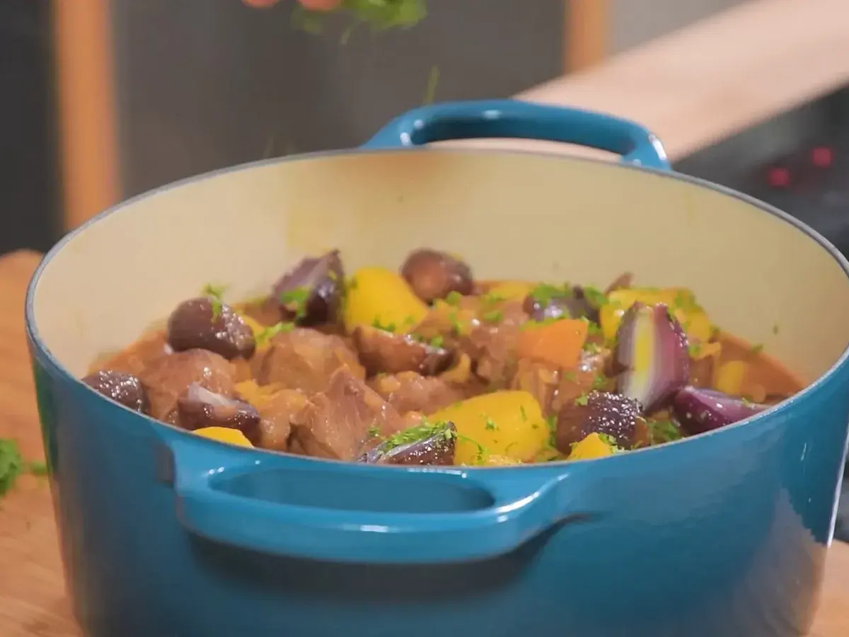Un plat mijoté de navarin d'agneau, avec des morceaux de viande tendres, des carottes, des oignons rouges et des pommes de terre, garni de persil frais.