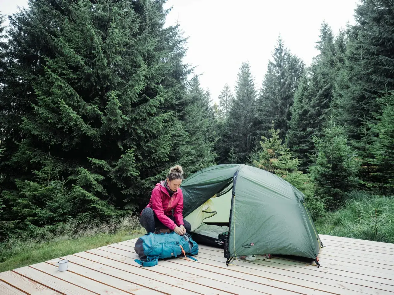 Une femme prépare son sac à dos près d'une tente dans une forêt de sapins. Une scène de camping en Allemagne.