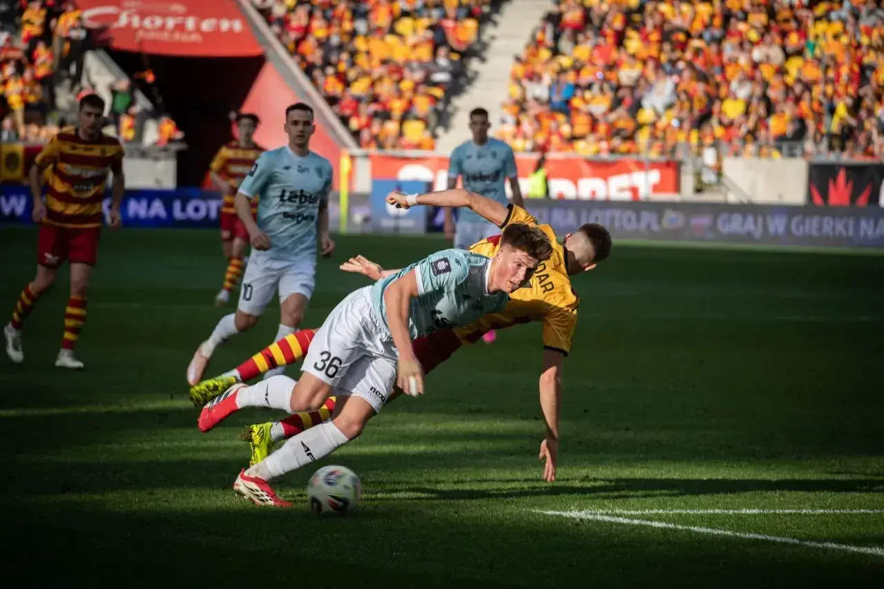 Zacięta walka o piłkę podczas meczu Jagiellonia Białystok – Piast Gliwice. Dwóch zawodników walczy o panowanie nad futbolówką na murawie.