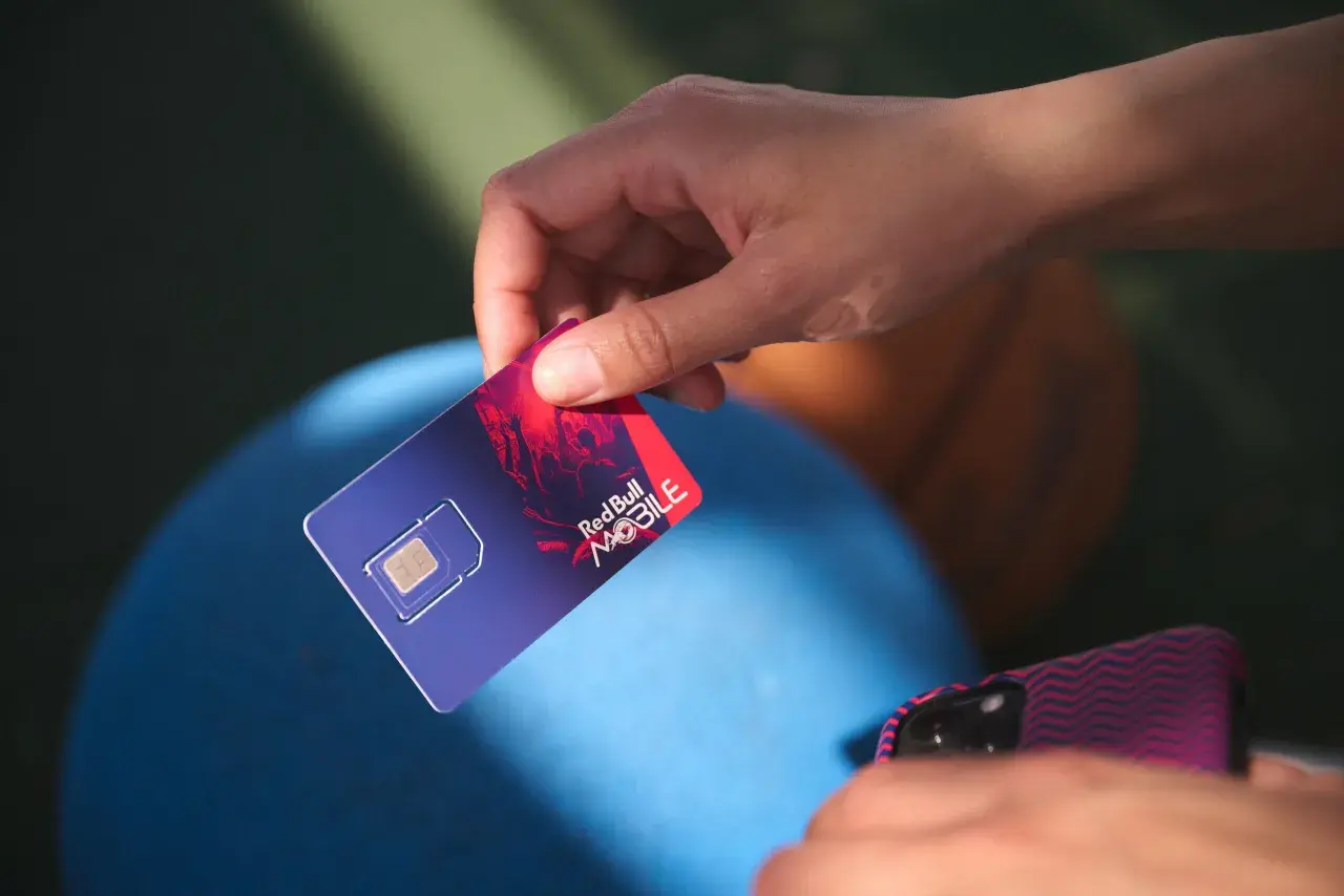Dłoń trzyma kartę SIM Red Bull MOBILE, gotową do podróży po Europie. Internet na wyciągnięcie ręki!