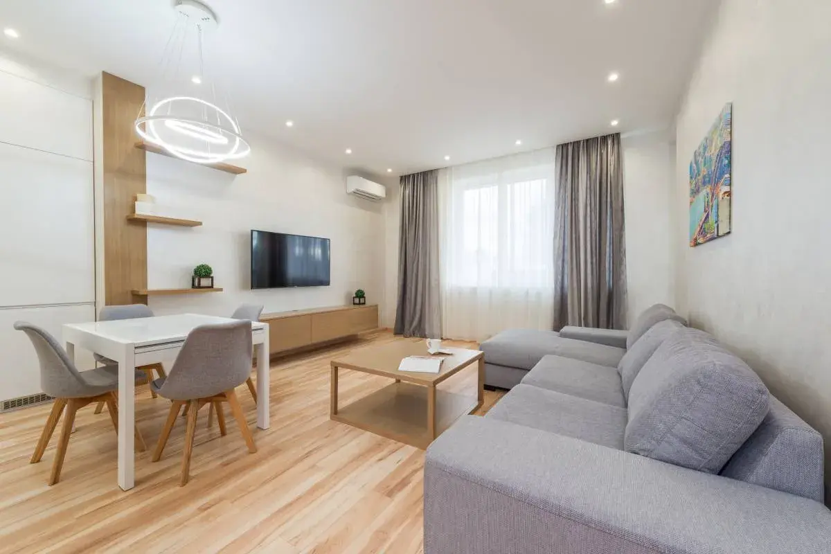 Elegante salón con sofá gris, mesa de comedor blanca y detalles en madera. Los colores del salón crean un ambiente acogedor y moderno.