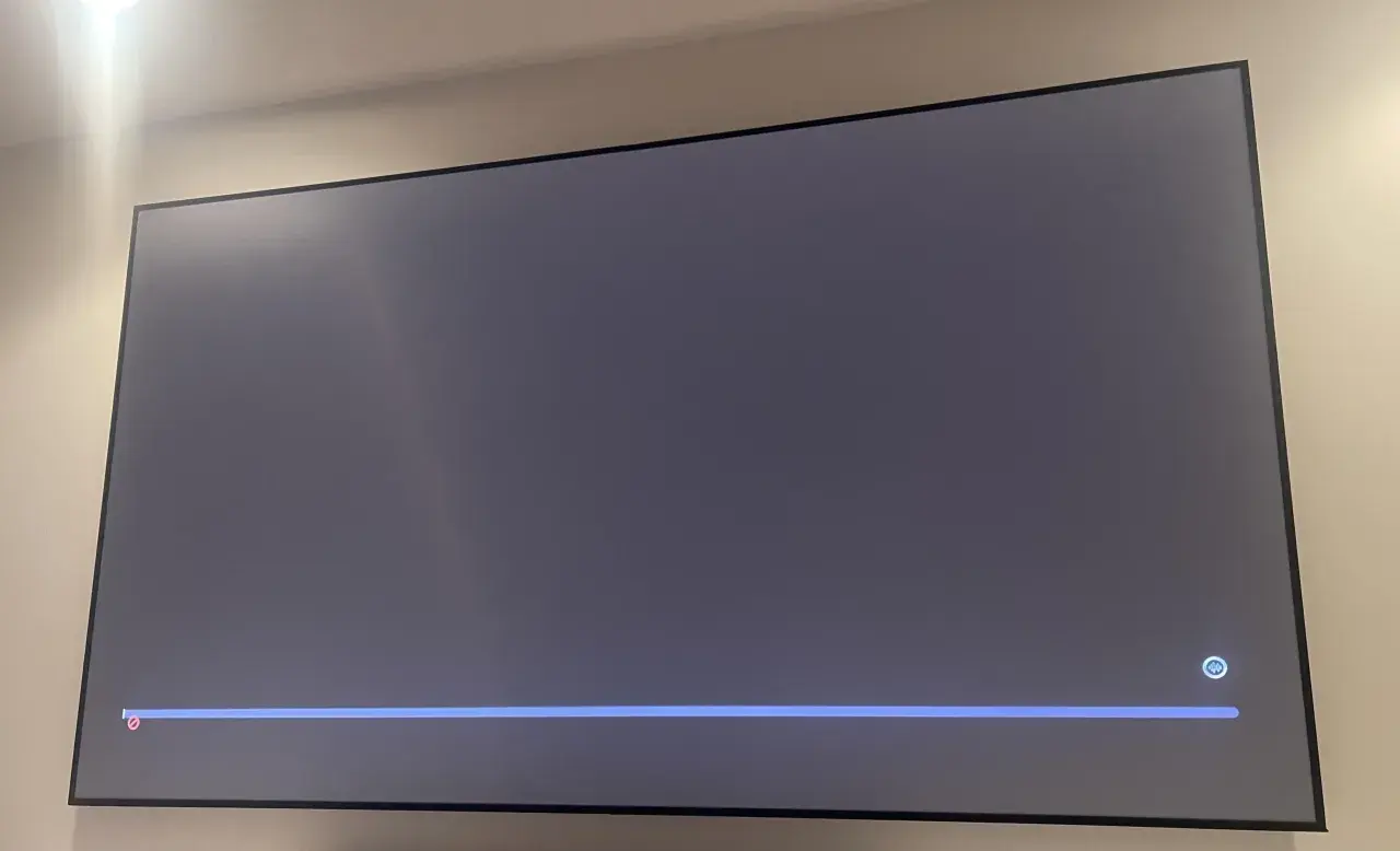 Szary ekran telewizora z niebieskim paskiem postępu i ikoną mikrofonu. Czekam na air play.
