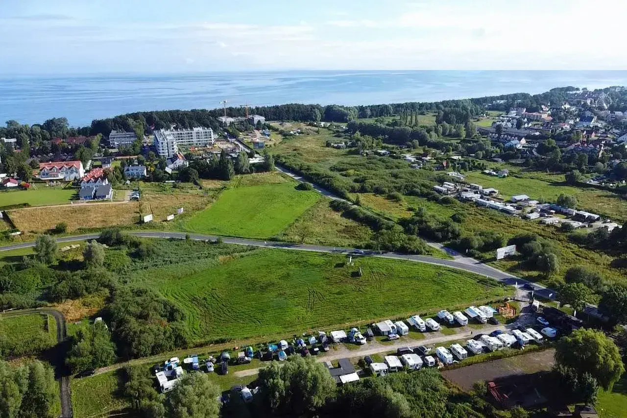 Widok z lotu ptaka na pole kempingowe w Kołobrzegu. Widać morze, zabudowania i wiele kamperów oraz przyczep kempingowych.